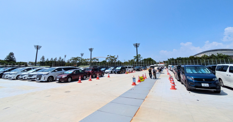 大阪万博会場周辺に整備された広々とした臨時駐車場に、整然と並ぶ車両と歩く来場者たち