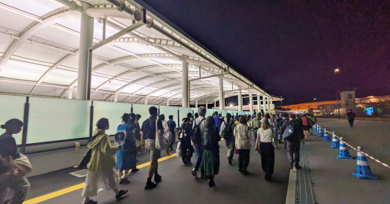 夜の大阪万博会場で、ライトアップされた通路を進む多くの来場者たちの様子