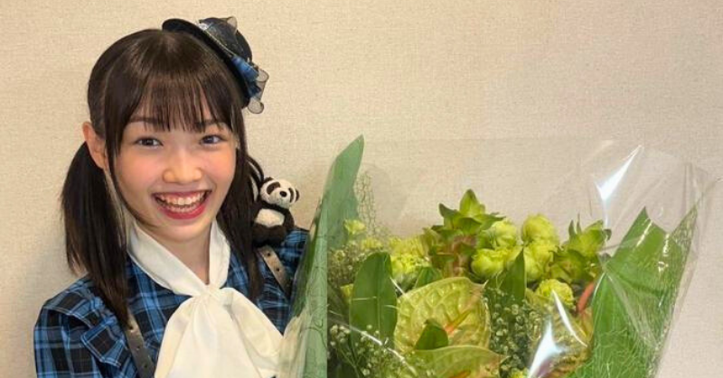 ツインテールの山崎愛生が笑顔で大きな花束を持っている。青いチェック柄の衣装に白いリボンをつけ、小さな帽子とぬいぐるみのパンダを肩に乗せている