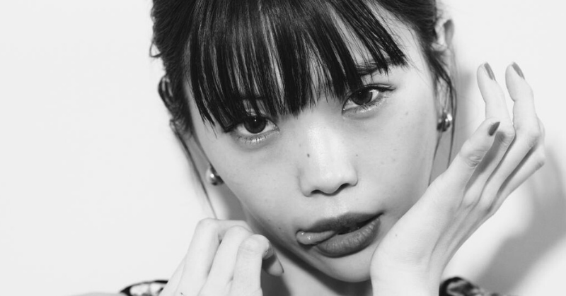 モノクロで撮影されたアイナジエンドのアップ写真。舌を少し出した挑発的な表情と鋭いまなざしが印象的なアーティスティックポートレート