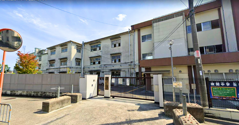 アイナジエンドが通っていたといわれる、正門と校舎が写る大阪府の豊中市立第四中学校の外観写真。晴れた日の校舎前で、門扉は閉まっている