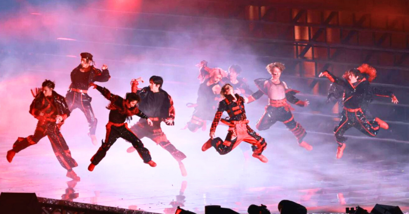 ステージ上でジャンプを決める9人組男性アイドルグループスノーマンが赤と黒の衣装をまとい、スモークと照明に包まれながら激しいパフォーマンスを披露している