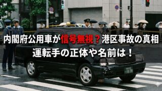 雨の交差点で、フロント部分が破損した黒いセダンの周囲に警察官が立ち、歩行者が傘をさして見守っている様子。画像上に「内閣府公用車が信号無視？港区事故の真相　運転手の正体や名前は！」という大きな文字が重ねられている。